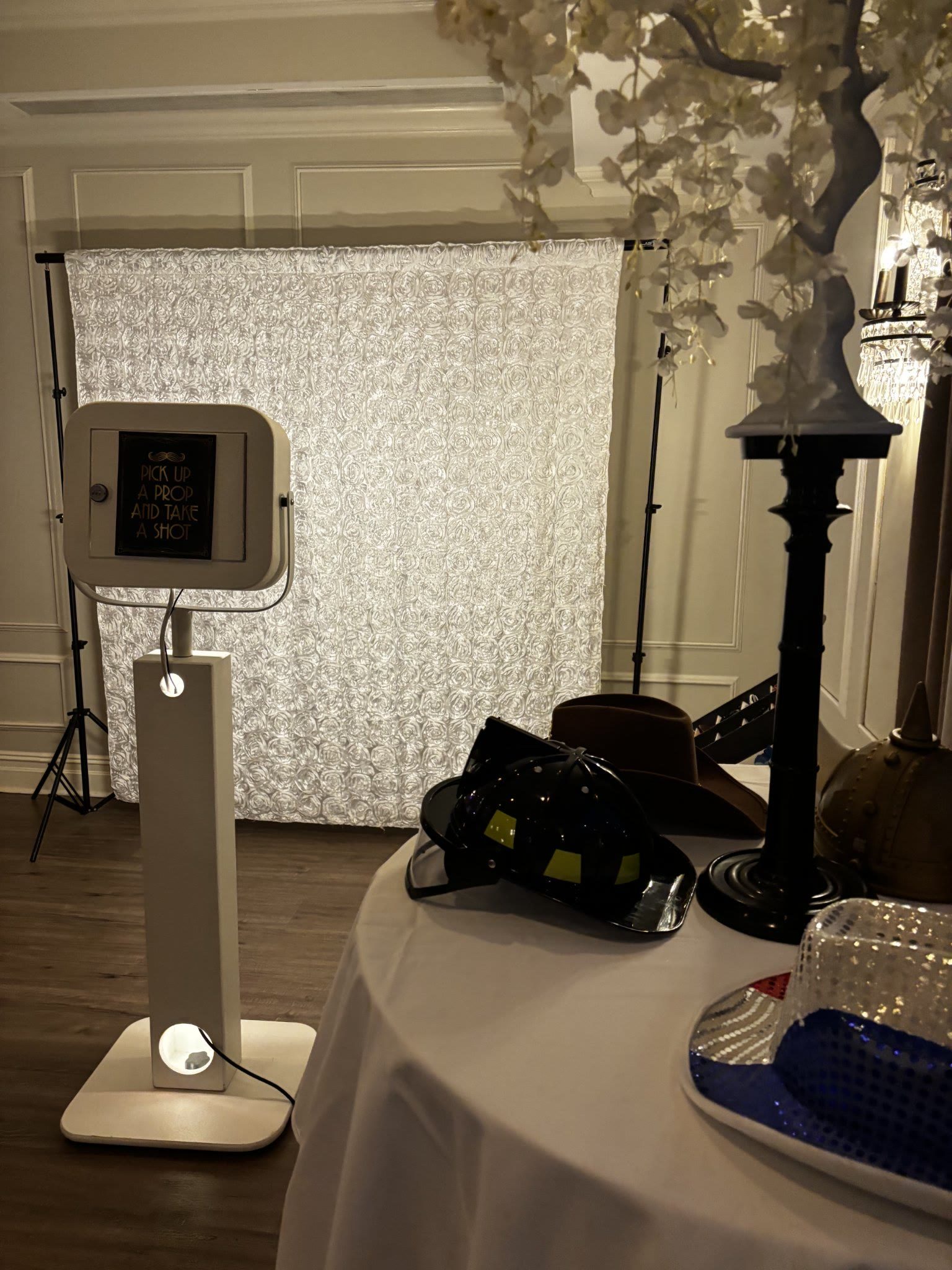 Selfie booth kiosk with elegant white backdrop and props table